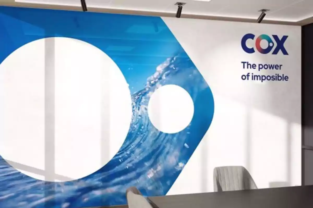 Mural en una sala de juntas con el logotipo de COX y el texto The power of imposible junto a un diseño azul con ondas de agua Mural en una sala de juntas con el logotipo de COX y el texto The power of imposible junto a un diseño azul con ondas de agua