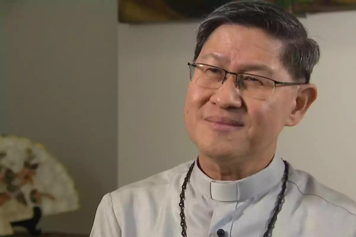 Un hombre con gafas y vestimenta clerical sonríe suavemente mientras mira hacia un lado.