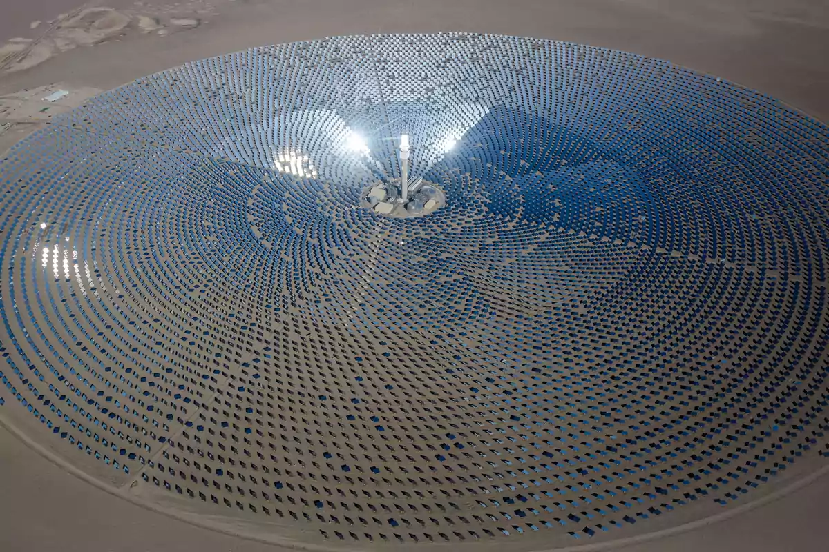 Vista aérea de una planta solar con numerosos paneles dispuestos en un patrón circular en el desierto.