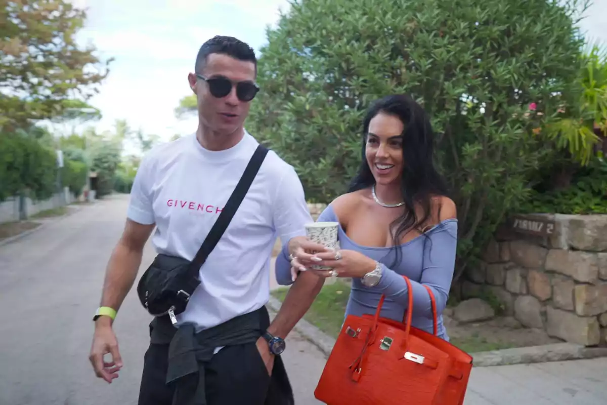 Cristina Ronaldo y Georgina Rodríguez caminando al aire libre, una de ellas lleva una camiseta blanca y gafas de sol, mientras que la otra sostiene una bebida y lleva un bolso naranja. Cristina Ronaldo y Georgina Rodríguez caminando al aire libre, una de ellas lleva una camiseta blanca y gafas de sol, mientras que la otra sostiene una bebida y lleva un bolso naranja.