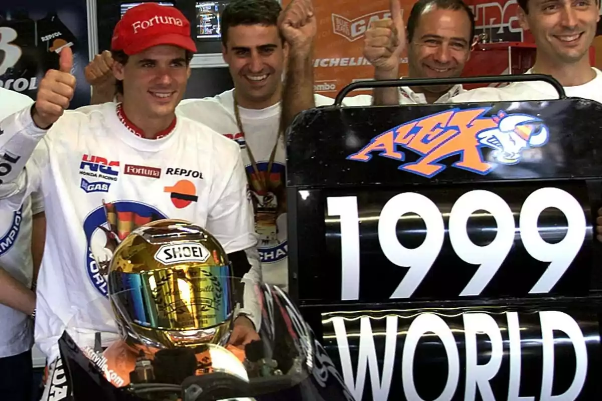 Un grupo de personas sonríe y levanta el pulgar junto a una motocicleta con un casco dorado y un cartel que dice 1999 World.