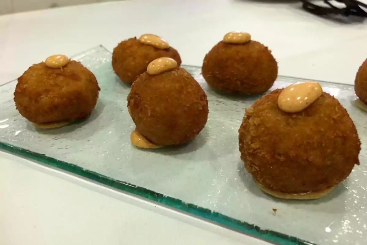 Croquetas doradas con salsa encima servidas en un plato de vidrio.