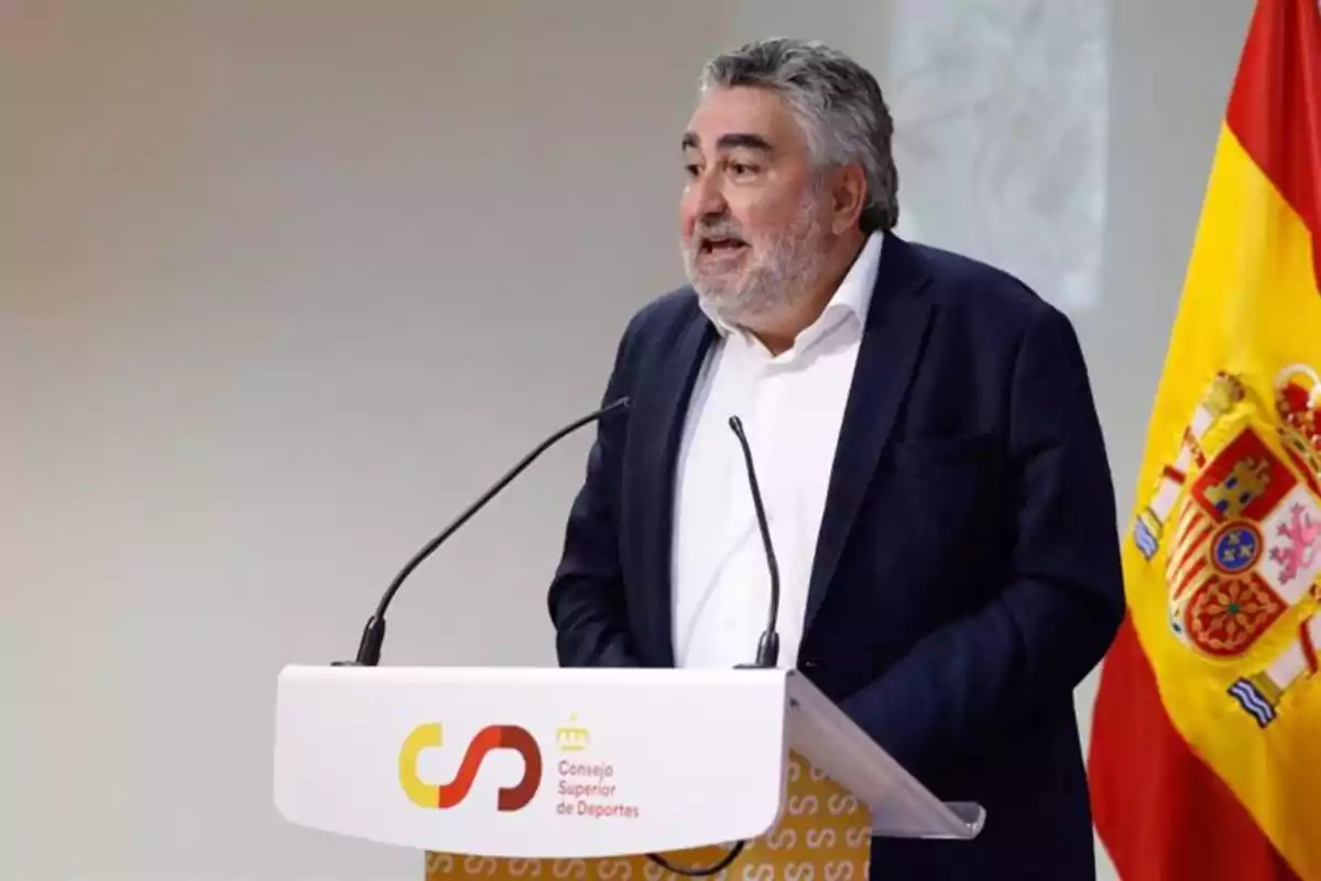 Un hombre de pie detrás de un podio con el logotipo del Consejo Superior de Deportes y la bandera de España a su lado.