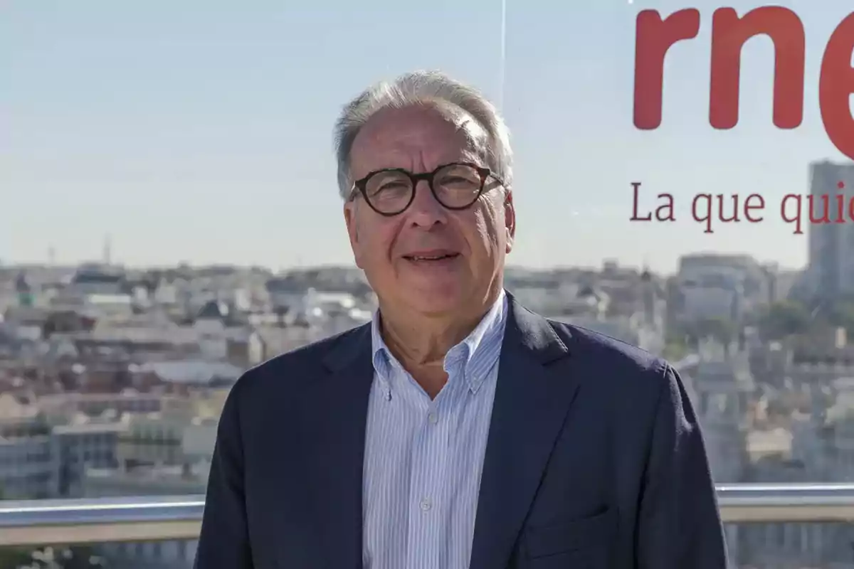 Un hombre con gafas y traje oscuro posando frente a un paisaje urbano. Un hombre con gafas y traje oscuro posando frente a un paisaje urbano.