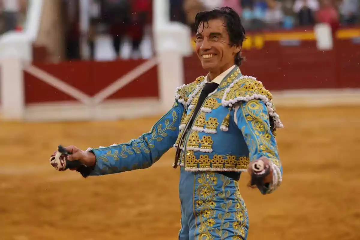 Un torero sonriente en la plaza de toros con traje azul y dorado.