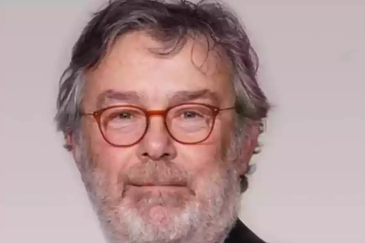 Hombre de cabello canoso y barba con gafas de montura redonda y fondo gris claro Hombre de cabello canoso y barba con gafas de montura redonda y fondo gris claro