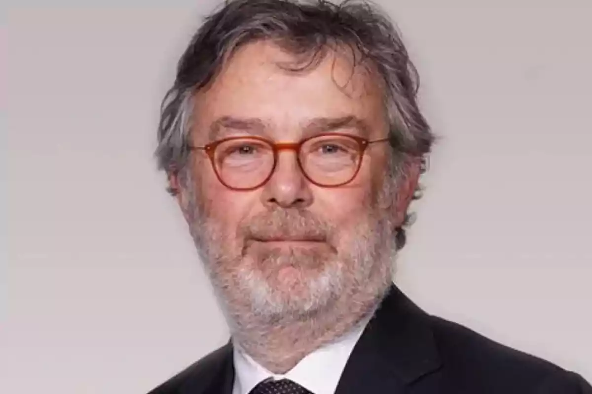 Hombre con gafas y barba gris vistiendo traje y corbata.