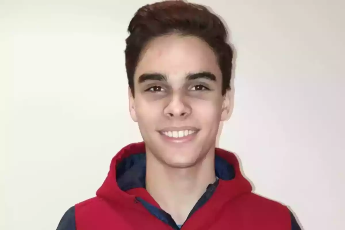 Joven sonriendo con sudadera roja y fondo claro.