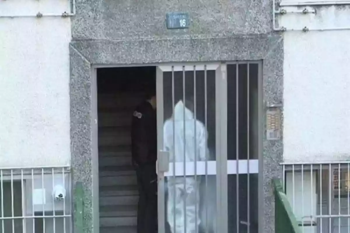 Una persona con traje de protección y un oficial de policía están en la entrada de un edificio con el número 16.