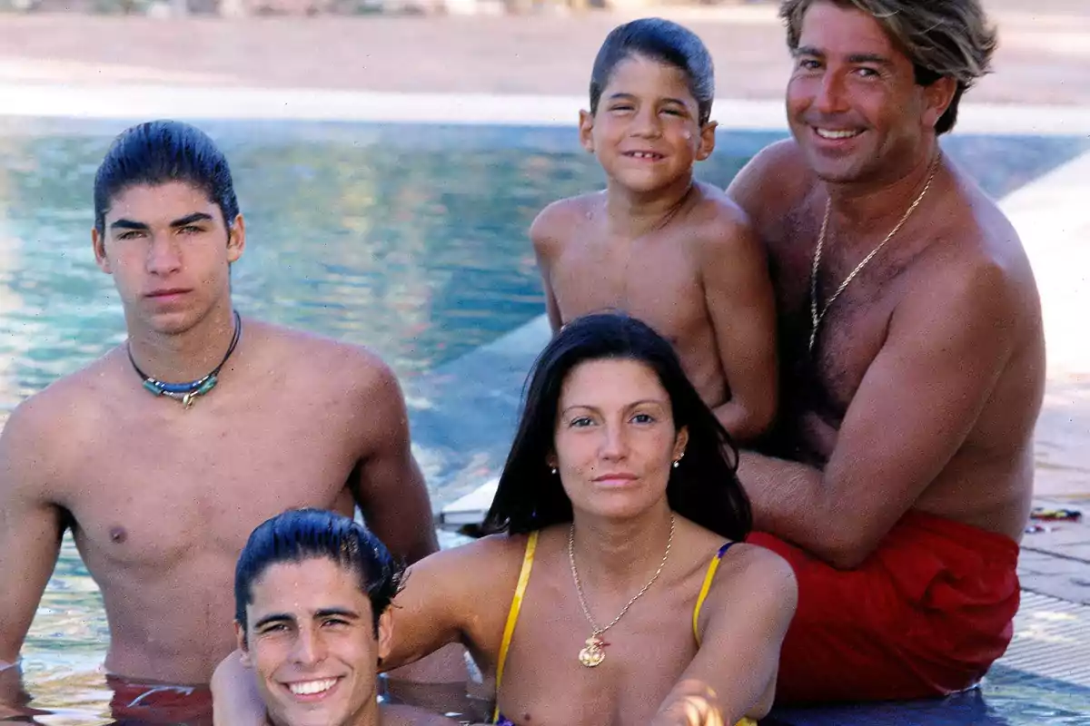 Una familia de cinco personas posando junto a una piscina, todos con trajes de baño y sonriendo.