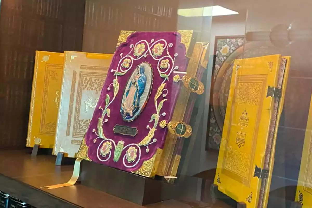 Libros antiguos con cubiertas decorativas y detalles dorados exhibidos en una vitrina.