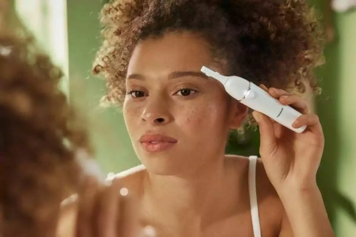 Una mujer usando una depiladora facial eléctrica de Lidl para dar forma a sus cejas frente a un espejo. Una mujer usando una depiladora facial eléctrica de Lidl para dar forma a sus cejas frente a un espejo.