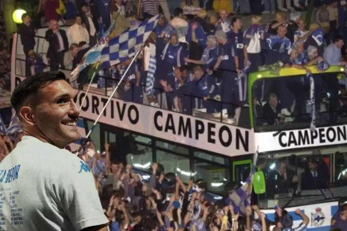 Un hombre sonriente con una camiseta blanca está frente a un autobús lleno de personas celebrando, con una bandera a cuadros y la palabra "CAMPEON" visible en el vehículo.