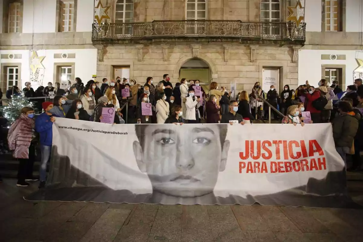 Un grupo de personas se manifiesta frente a un edificio sosteniendo una pancarta grande con el rostro de una mujer y el mensaje Justicia para Deborah mientras otras personas sostienen carteles morados y usan mascarillas Un grupo de personas se manifiesta frente a un edificio sosteniendo una pancarta grande con el rostro de una mujer y el mensaje Justicia para Deborah mientras otras personas sostienen carteles morados y usan mascarillas