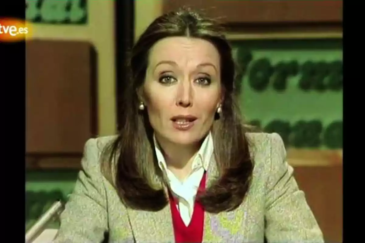 Una mujer con cabello largo y suelto, vestida con un suéter rojo y una chaqueta gris, aparece en un set de televisión con el logotipo de rtve.es en la esquina superior izquierda.