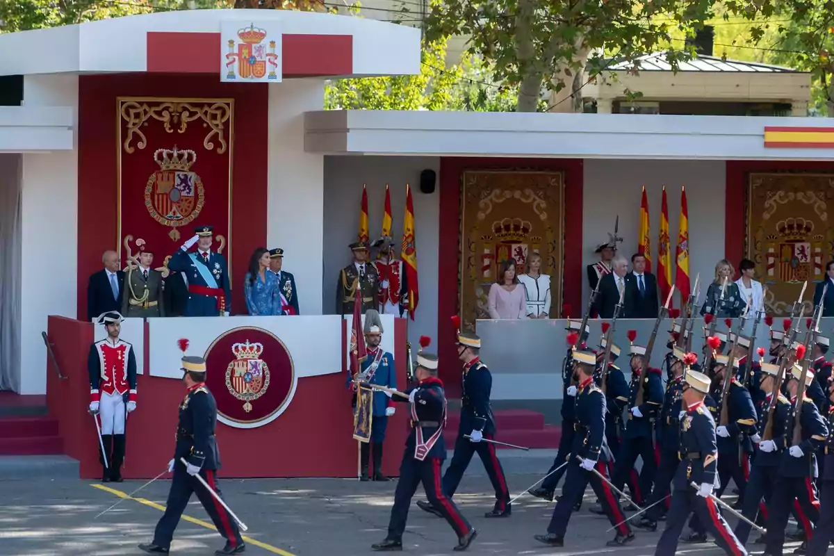 Un desfile militar con oficiales y dignatarios en una plataforma decorada con emblemas y banderas de España.