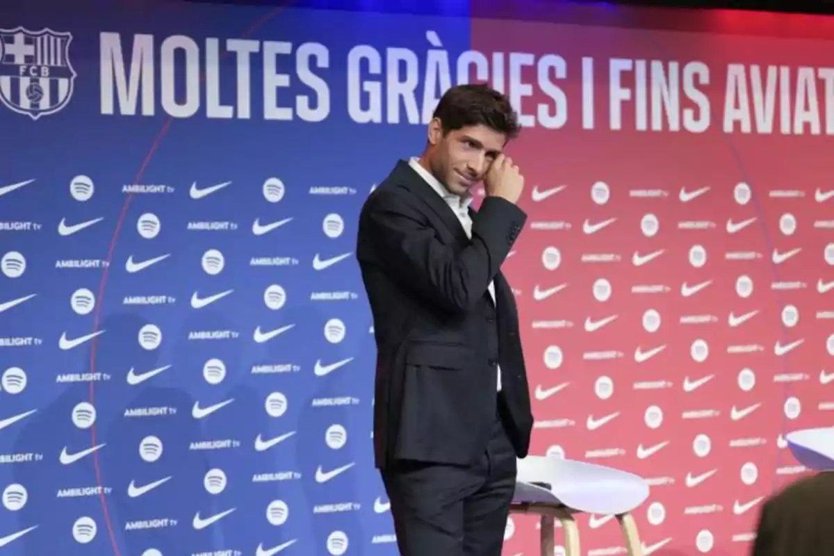 Un hombre en traje oscuro se limpia una lágrima en un escenario con un fondo de logotipos de Nike, Spotify y Ambilight TV, junto a un mensaje de agradecimiento en catalán.