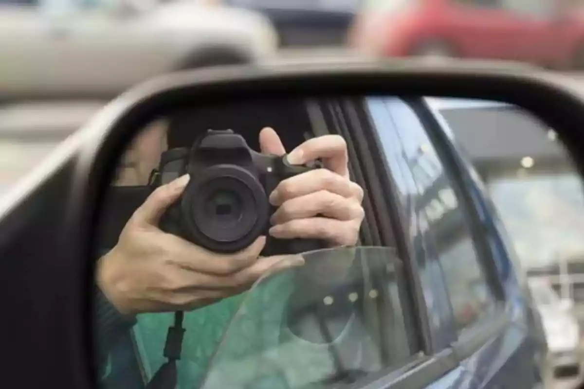 Persona sosteniendo una cámara reflejada en el espejo lateral de un automóvil.