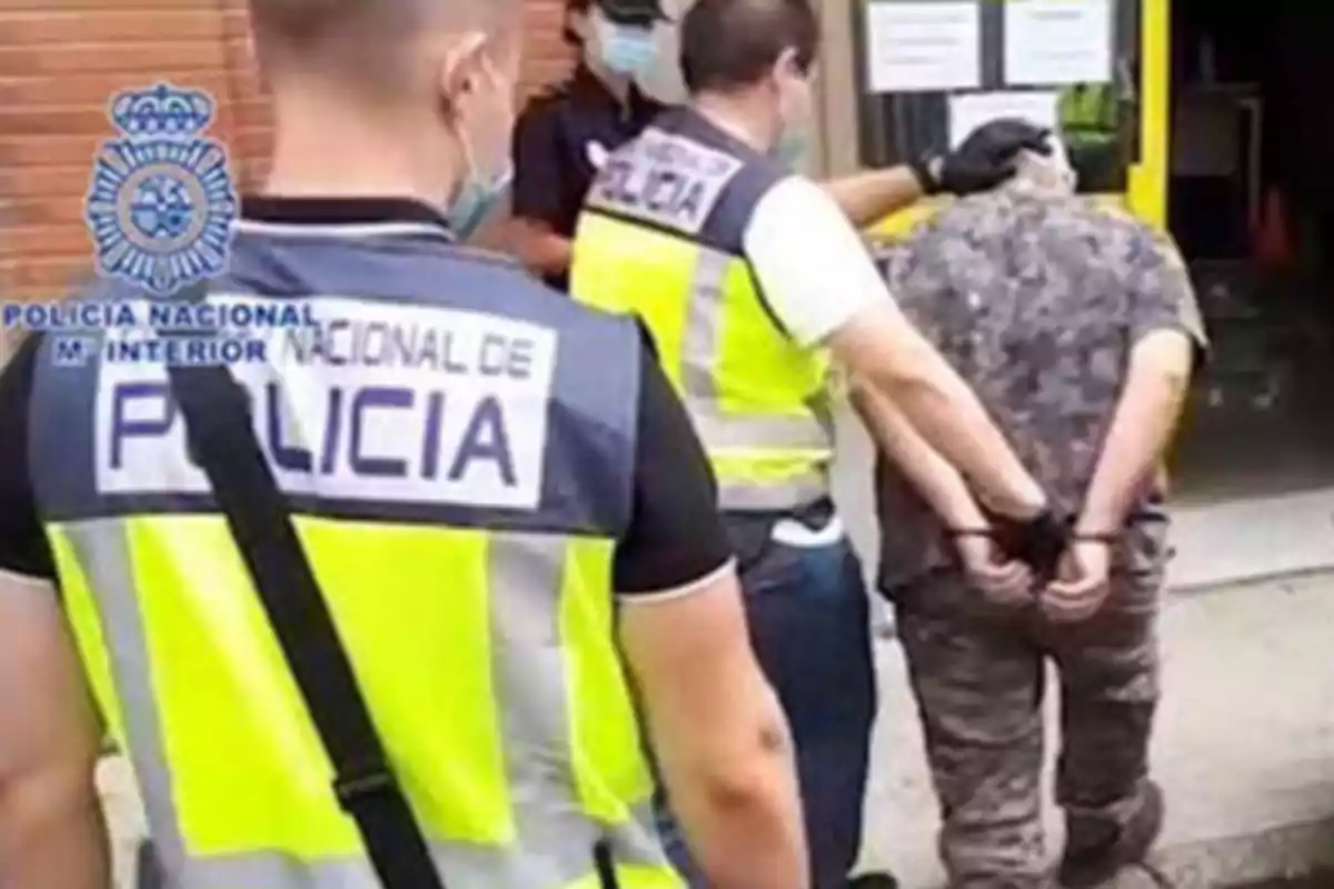 Policías arrestando a una persona esposada frente a un edificio.