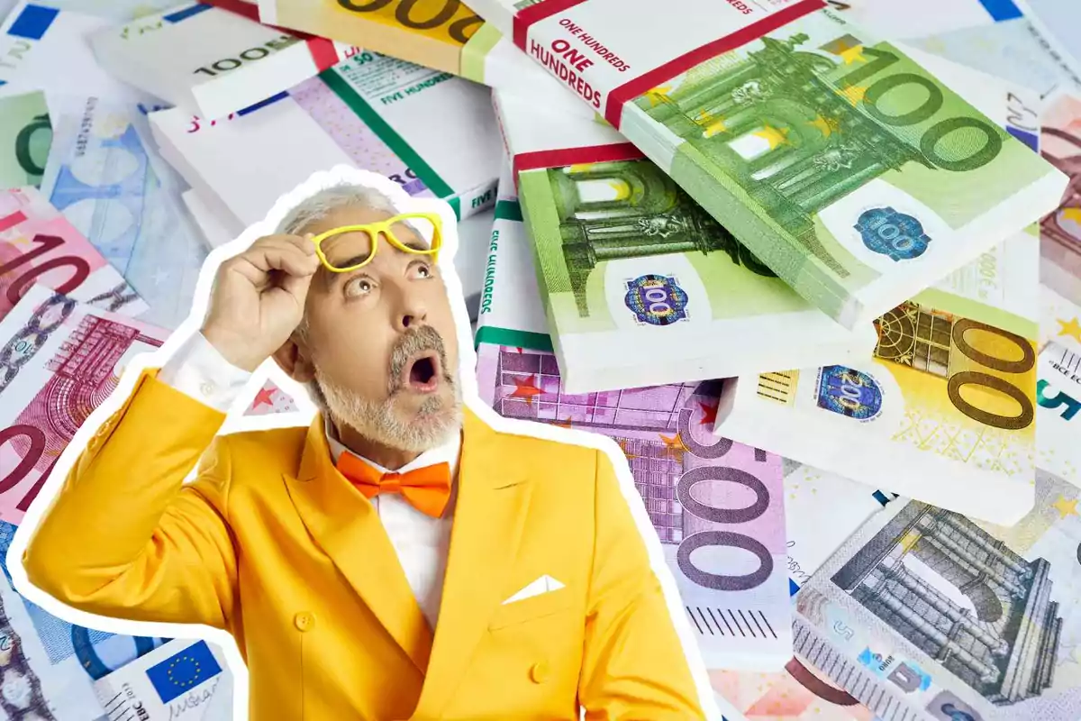 Un hombre con traje amarillo y gafas amarillas parece sorprendido mientras mira hacia arriba, con una gran cantidad de billetes de euro apilados detrás de él.