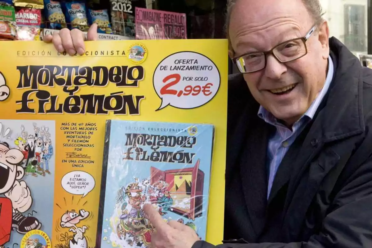 Un hombre sonriente sostiene un cartel promocional de una edición coleccionista de "Mortadelo y Filemón" con una oferta de lanzamiento por 2,99€.