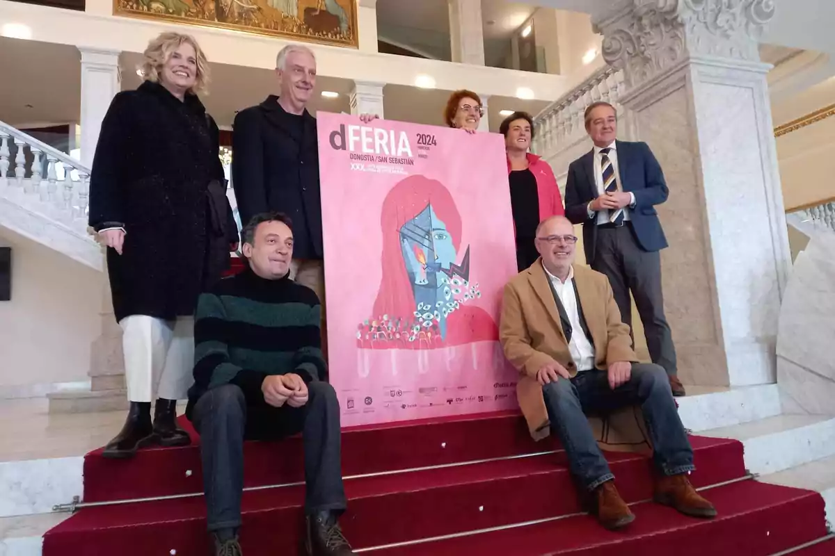 Un grupo de personas posando en una escalera junto a un cartel de la feria dFERIA 2024 en Donostia/San Sebastián.