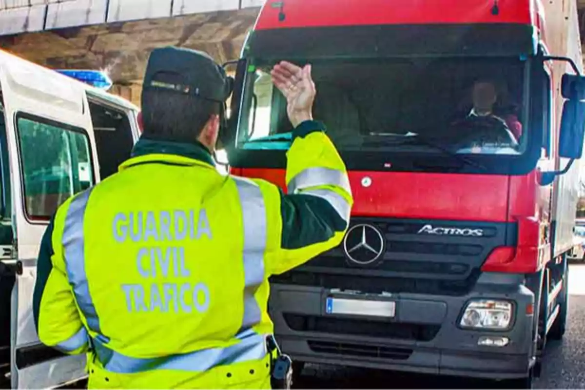 Un agente de la Guardia Civil de Tráfico está deteniendo un camión rojo en la carretera.