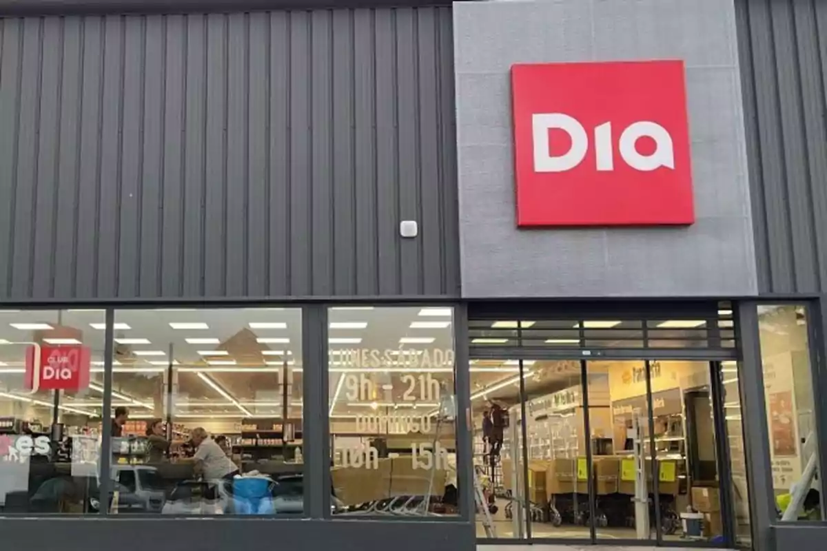 Fachada de una tienda de la cadena de supermercados Dia con el logotipo rojo y blanco en la parte superior derecha y ventanas que muestran el interior del establecimiento.