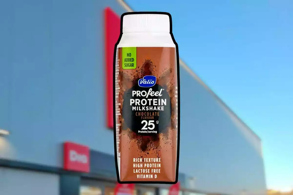 Una botella de batido de proteínas con sabor a chocolate, sin azúcar añadido, frente a un edificio con cielo azul de fondo. Una botella de batido de proteínas con sabor a chocolate, sin azúcar añadido, frente a un edificio con cielo azul de fondo.