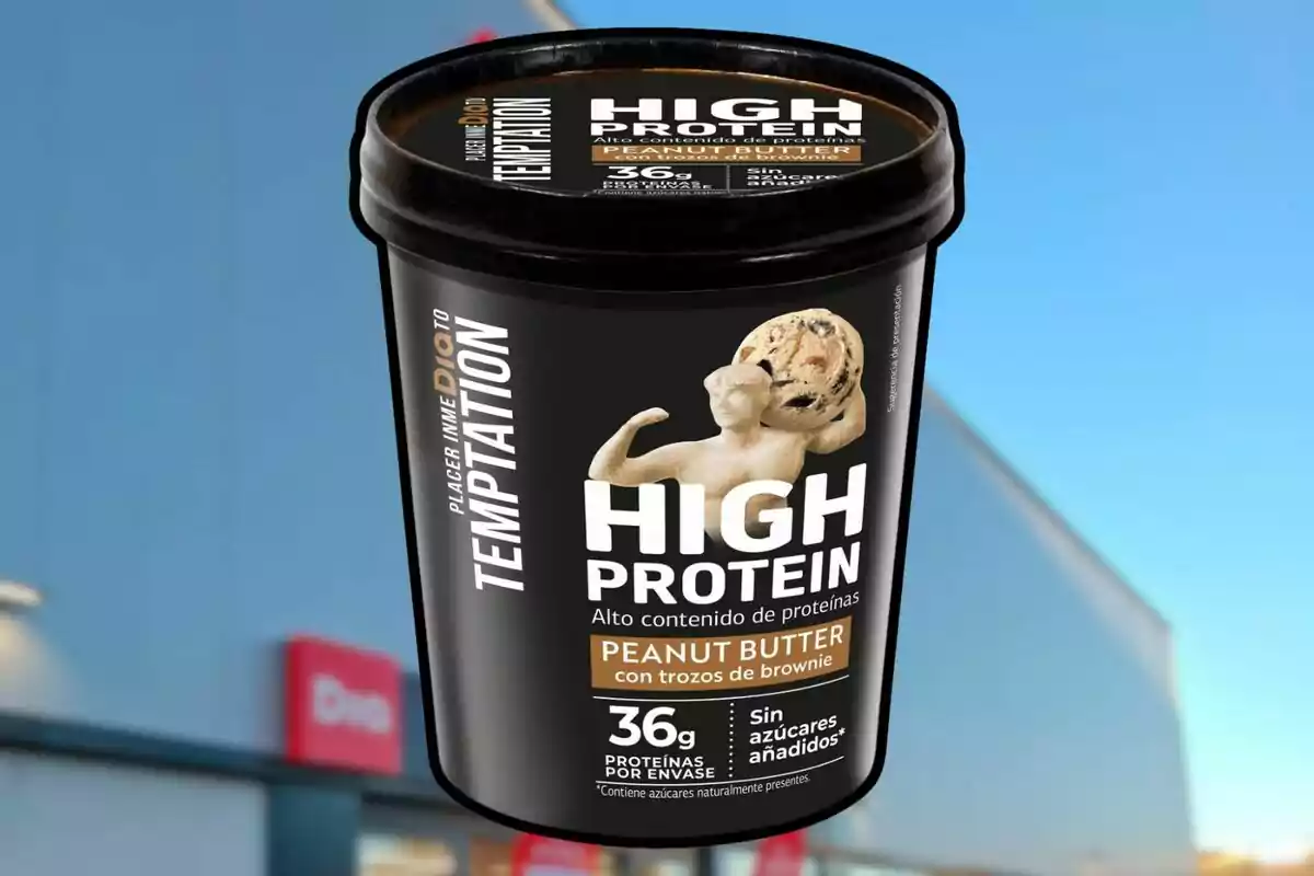 Envase de helado de alto contenido proteico con sabor a mantequilla de maní y trozos de brownie, con 36 gramos de proteínas por envase y sin azúcares añadidos, sobre un fondo de cielo azul y edificio. Envase de helado de alto contenido proteico con sabor a mantequilla de maní y trozos de brownie, con 36 gramos de proteínas por envase y sin azúcares añadidos, sobre un fondo de cielo azul y edificio.