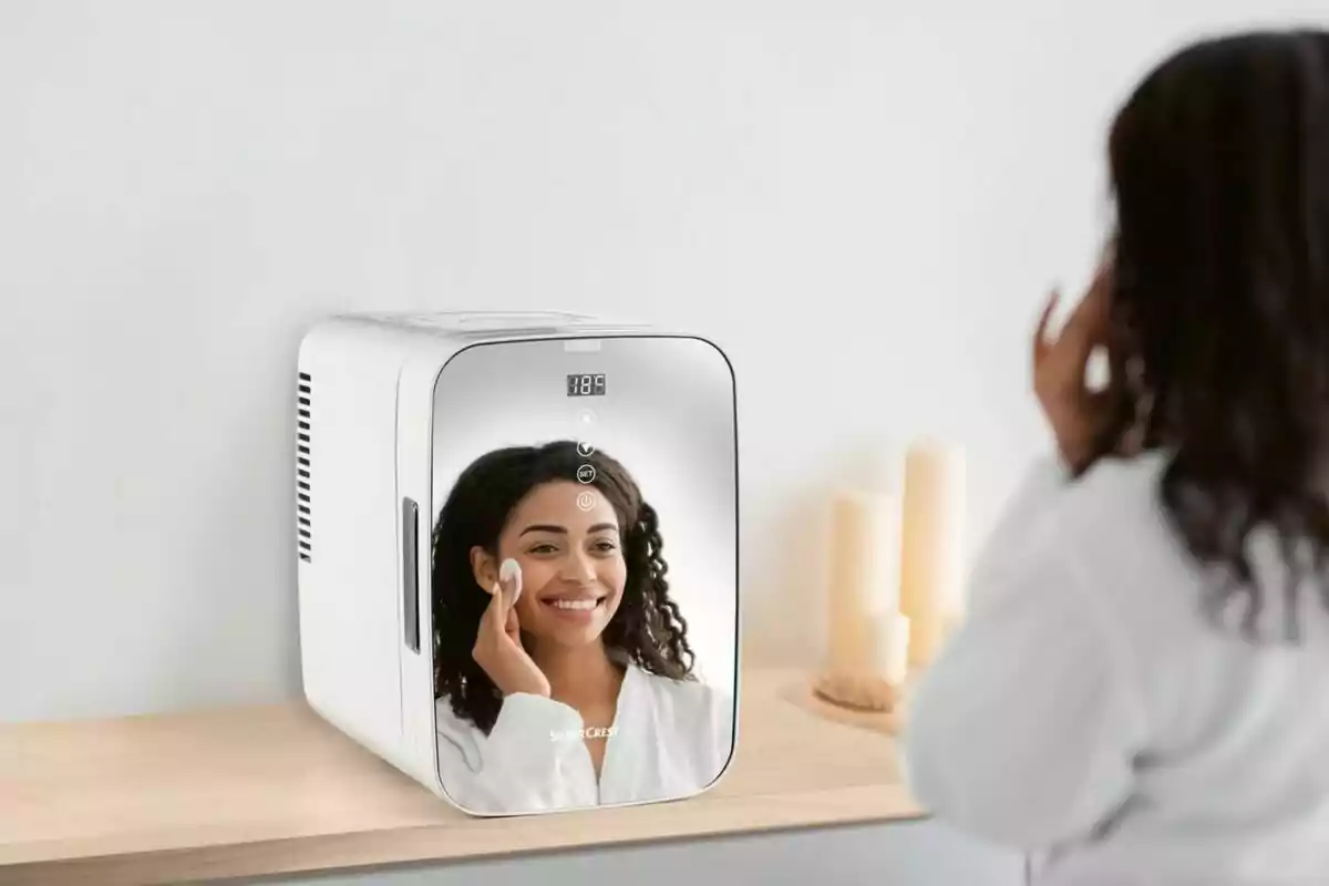 Una mujer se mira en el espejo de un mini refrigerador mientras se aplica un producto facial con un algodón en un ambiente minimalista con velas al fondo Una mujer se mira en el espejo de un mini refrigerador mientras se aplica un producto facial con un algodón en un ambiente minimalista con velas al fondo