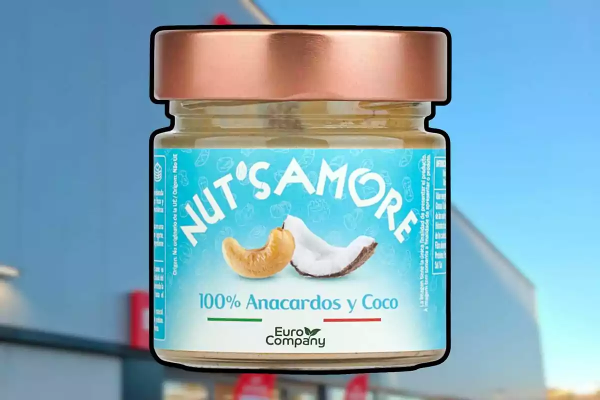 Un frasco de vidrio con tapa dorada que contiene una crema de anacardos y coco de la marca Nut's Amore, con un diseño de etiqueta azul claro que muestra imágenes de anacardos y coco. Un frasco de vidrio con tapa dorada que contiene una crema de anacardos y coco de la marca Nut's Amore, con un diseño de etiqueta azul claro que muestra imágenes de anacardos y coco.