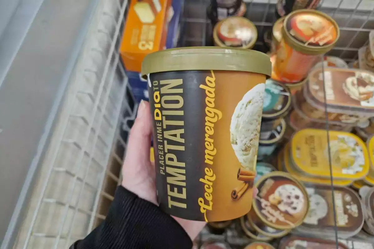 Envase de helado de leche merengada con canela de la marca Temptation sostenido por una mano en un supermercado. Envase de helado de leche merengada con canela de la marca Temptation sostenido por una mano en un supermercado.