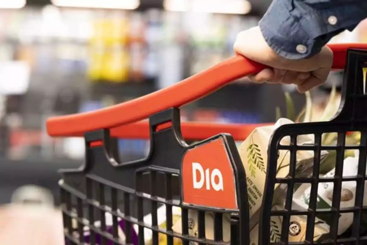 Persona empujando un carrito de compras en un supermercado con productos dentro.