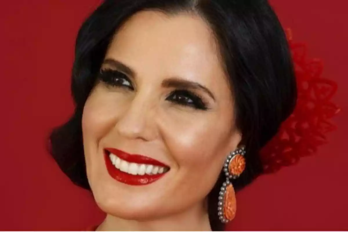 Mujer sonriente con labios rojos, pendientes naranjas y fondo rojo Mujer sonriente con labios rojos, pendientes naranjas y fondo rojo