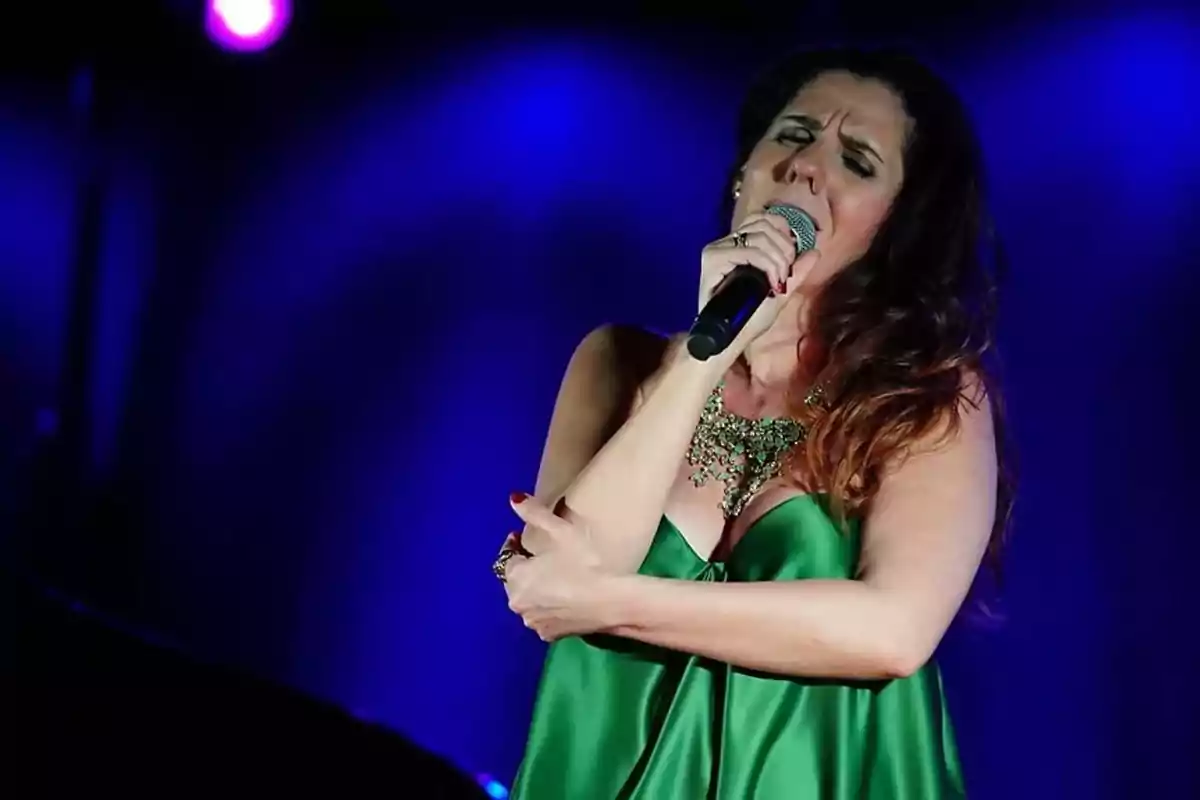 Mujer cantando apasionadamente en el escenario con vestido verde y fondo iluminado en tonos morados