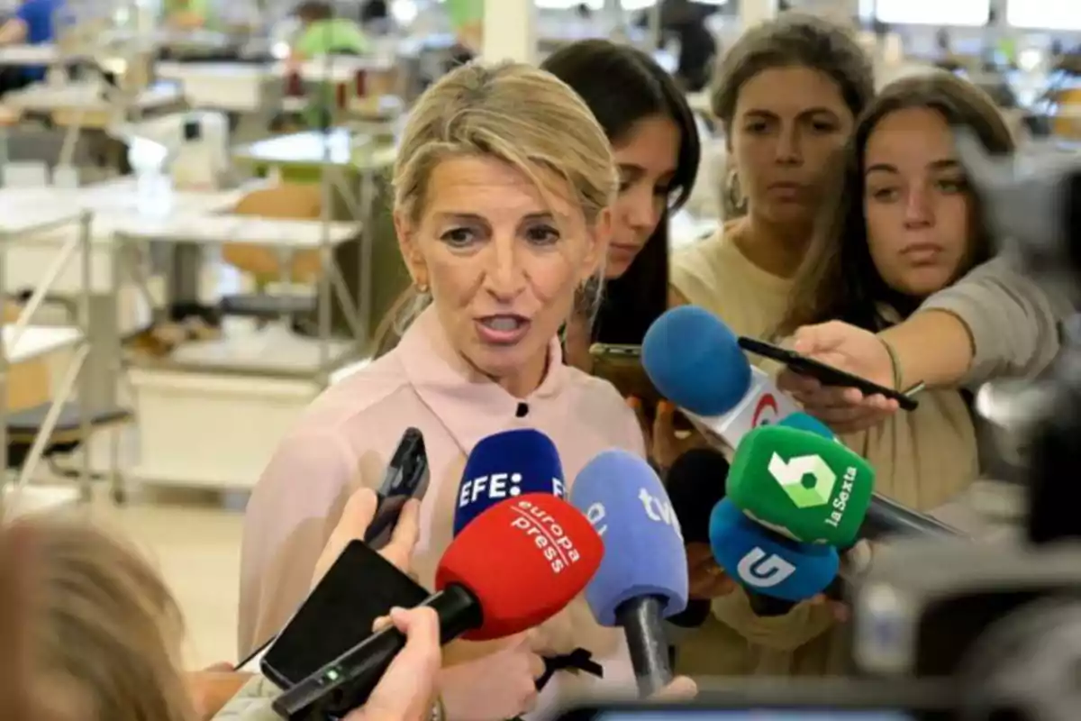 Una mujer hablando frente a varios micrófonos de diferentes medios de comunicación en un entorno de trabajo.