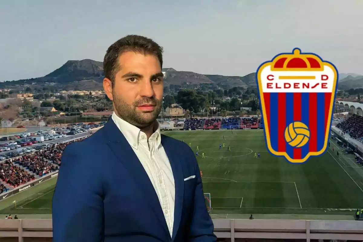Hombre con traje azul posando frente a un estadio de fútbol lleno de espectadores y el escudo del club Deportivo Eldense a la derecha