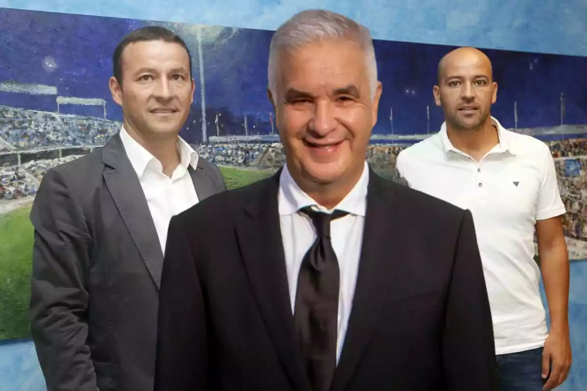 Tres hombres posan frente a una pintura de un estadio, el hombre en primer plano lleva traje y corbata, mientras que los otros dos están en segundo plano, uno con saco y el otro con camiseta polo blanca. Tres hombres posan frente a una pintura de un estadio, el hombre en primer plano lleva traje y corbata, mientras que los otros dos están en segundo plano, uno con saco y el otro con camiseta polo blanca.