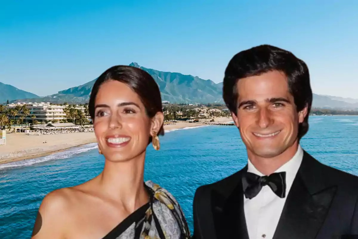 Una mujer y un hombre sonrientes posando frente a una playa con montañas al fondo.