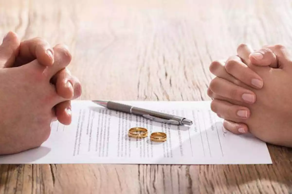 Las manos de un hombre y una mujer, enfrentadas, con un papel de divorcio en medio. Encima, dos anillos y un bolígrafo.