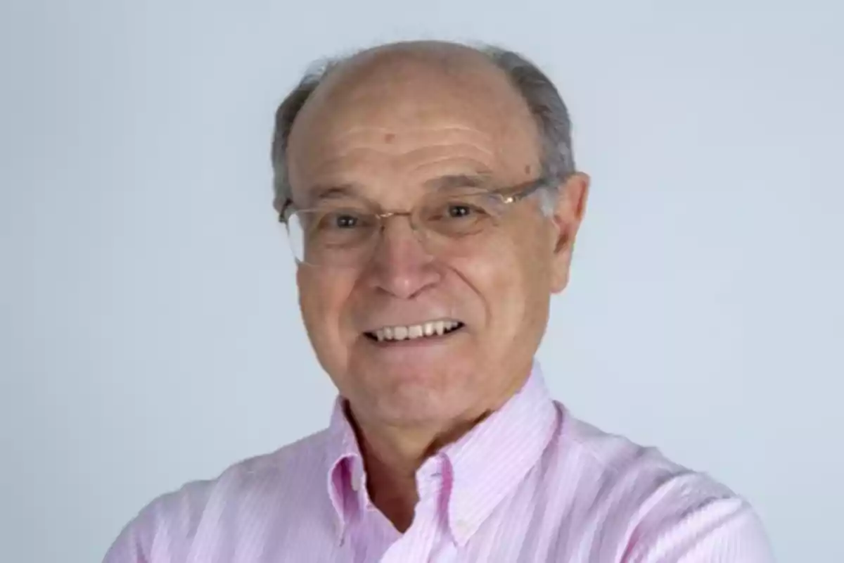 Hombre mayor con camisa a rayas rosadas y gafas sonriendo frente a un fondo claro.