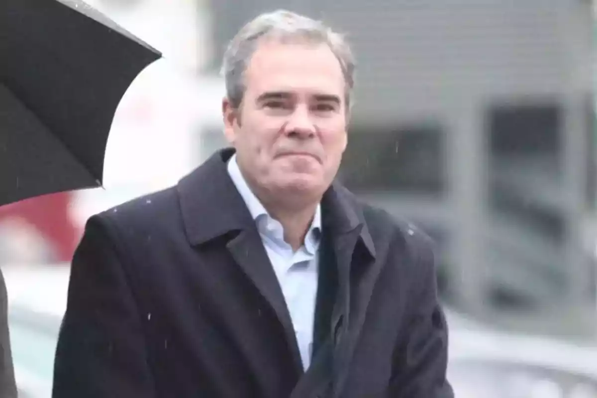 Hombre de cabello canoso con abrigo oscuro caminando bajo la lluvia junto a un paraguas negro Hombre de cabello canoso con abrigo oscuro caminando bajo la lluvia junto a un paraguas negro