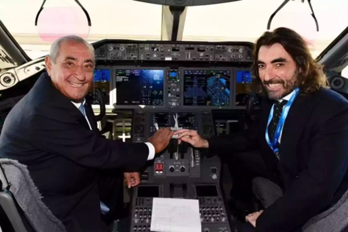 Dos hombres sonrientes en la cabina de un avión, uno de ellos sostiene un modelo de avión.