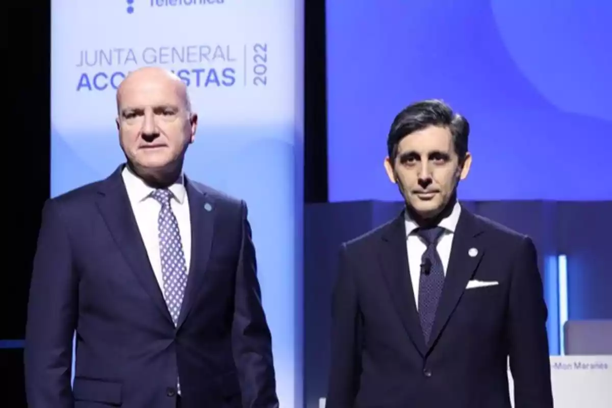 Dos hombres con traje posan en un escenario corporativo con un fondo que muestra el texto Junta General Accionistas 2022.