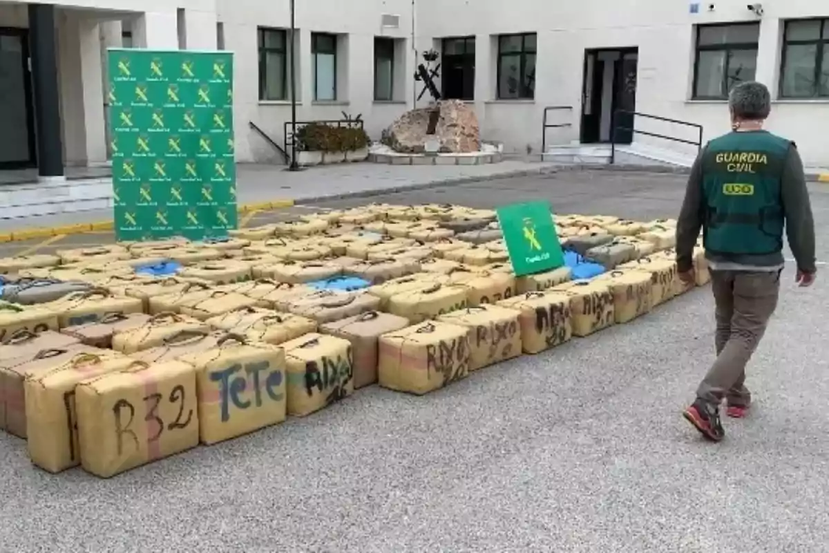 Un agente de la Guardia Civil camina junto a numerosos paquetes apilados en el suelo frente a un edificio oficial.