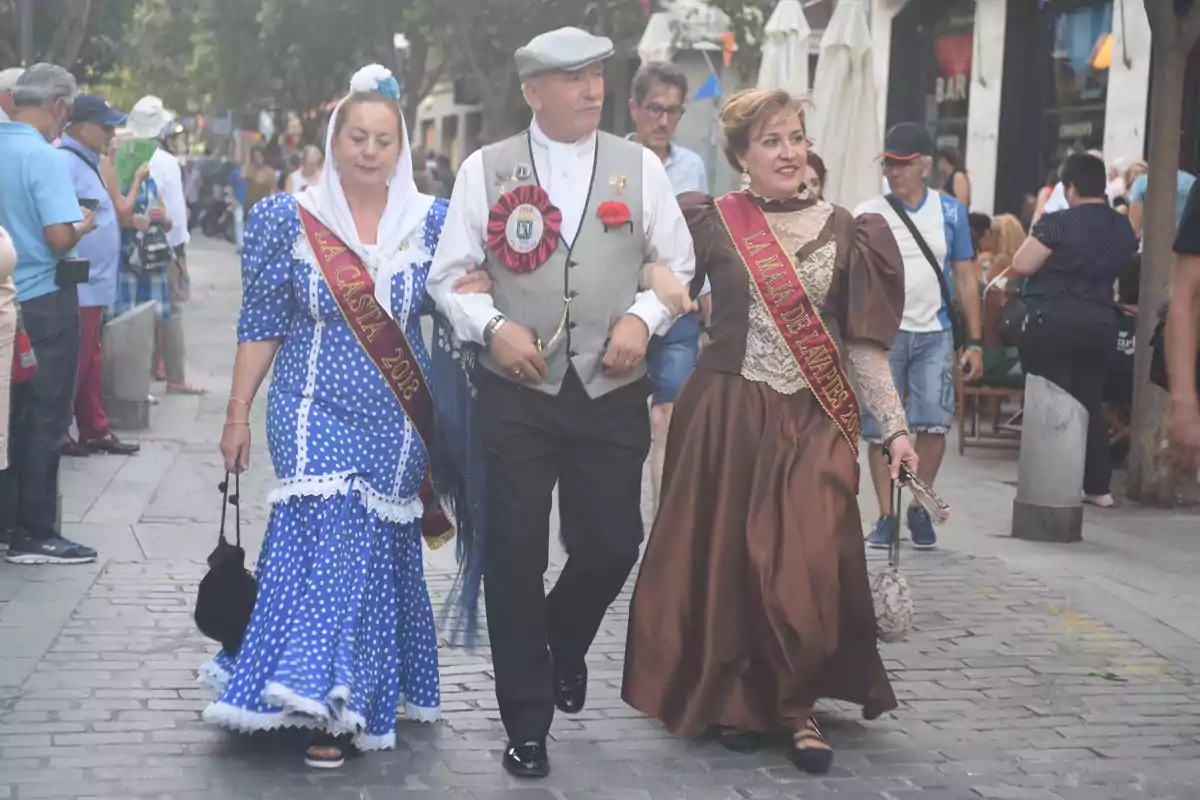 Personas vestidas con trajes tradicionales caminando por una calle concurrida durante un evento festivo.