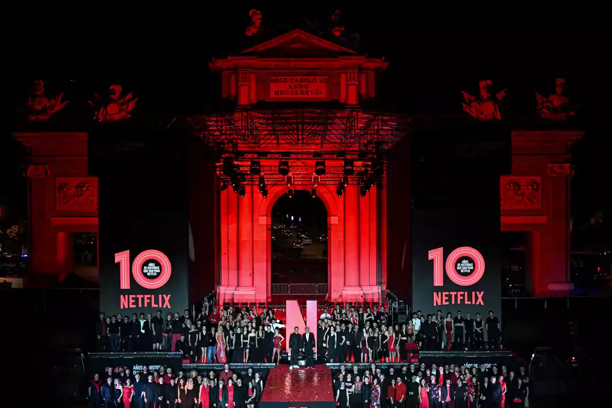 Celebración nocturna del décimo aniversario de Netflix en España con un gran grupo de personas frente a la Puerta de Alcalá iluminada de rojo y decoraciones alusivas a la plataforma.