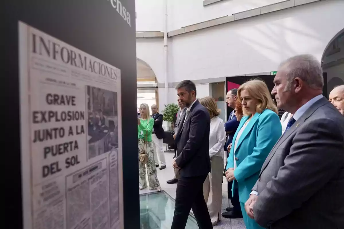 Un grupo de personas observa una exhibición que incluye una portada de periódico con el titular 