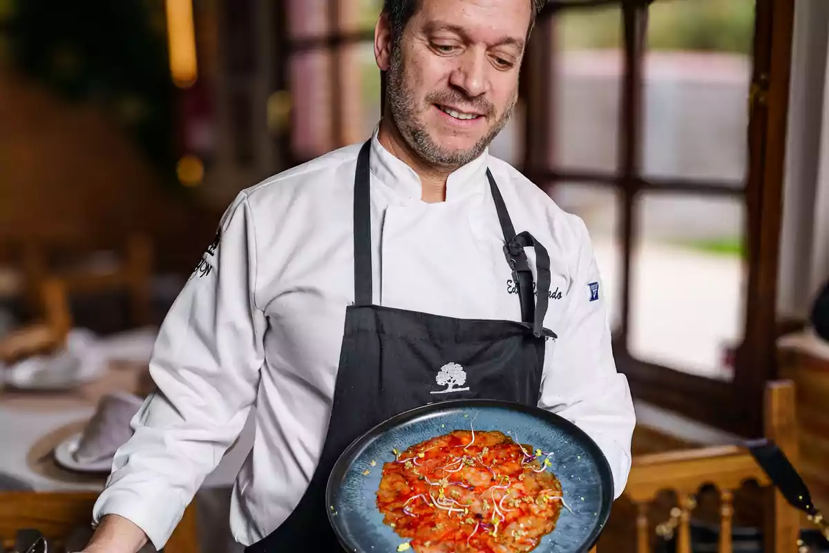 Un chef sonriente sostiene un plato con una preparación colorida en un restaurante acogedor.